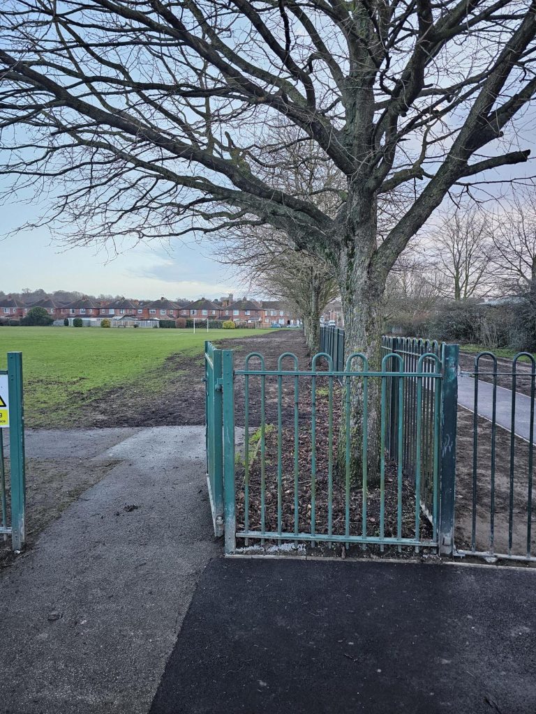 A section of the green Levellings gate, showing a section of the new tarmarcked footpath in front of it.
